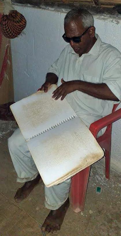 Blind Indian man reading worn copy of Braille